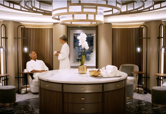Woman in spa robe talking to seated man in bathrobe.
