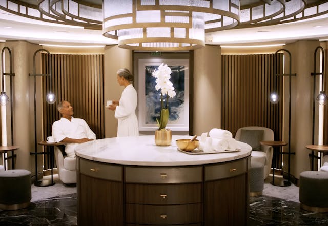 Woman in spa robe talking to seated man in bathrobe.