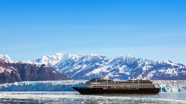 Cruise ship sailing in water with icebergs and mountains in background