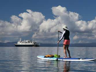 person stand up paddleboarding in ocean with uncruise ship in background