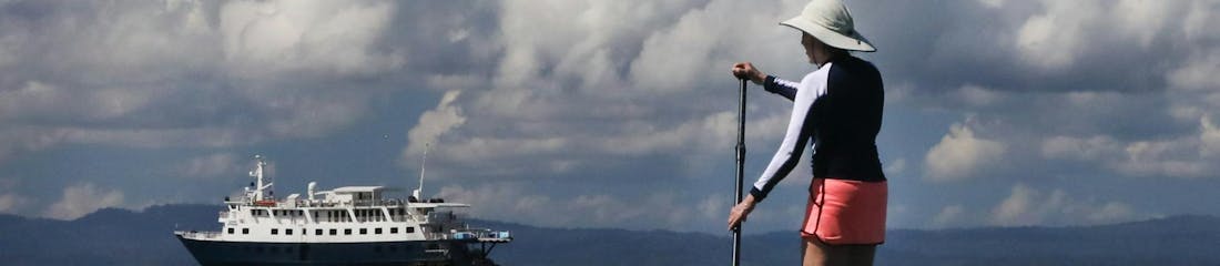 person stand up paddleboarding in ocean with uncruise ship in background