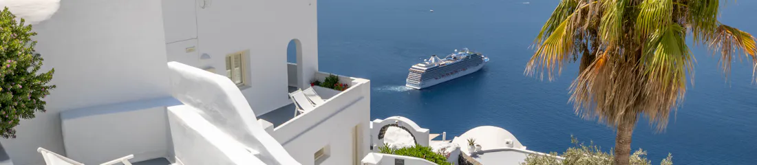 White Santorini terraces, stairs and pool overlooking Aegean Sea with cruise ship and palm tree.