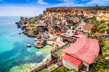 Colorful seaside village with red roofs, wooden walkways and turquoise bay with boats beside cliffs