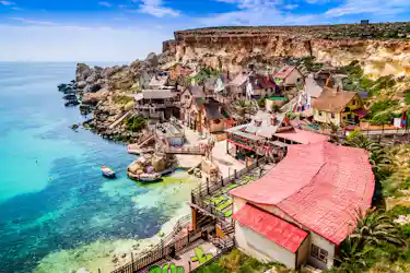 Colorful seaside village with red roofs, wooden walkways and turquoise bay with boats beside cliffs