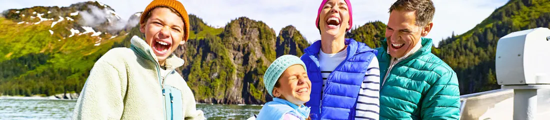 Laughing family in colorful jackets on a sightseeing boat near green mountain cliffs