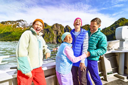 Laughing family in colorful jackets on a sightseeing boat near green mountain cliffs