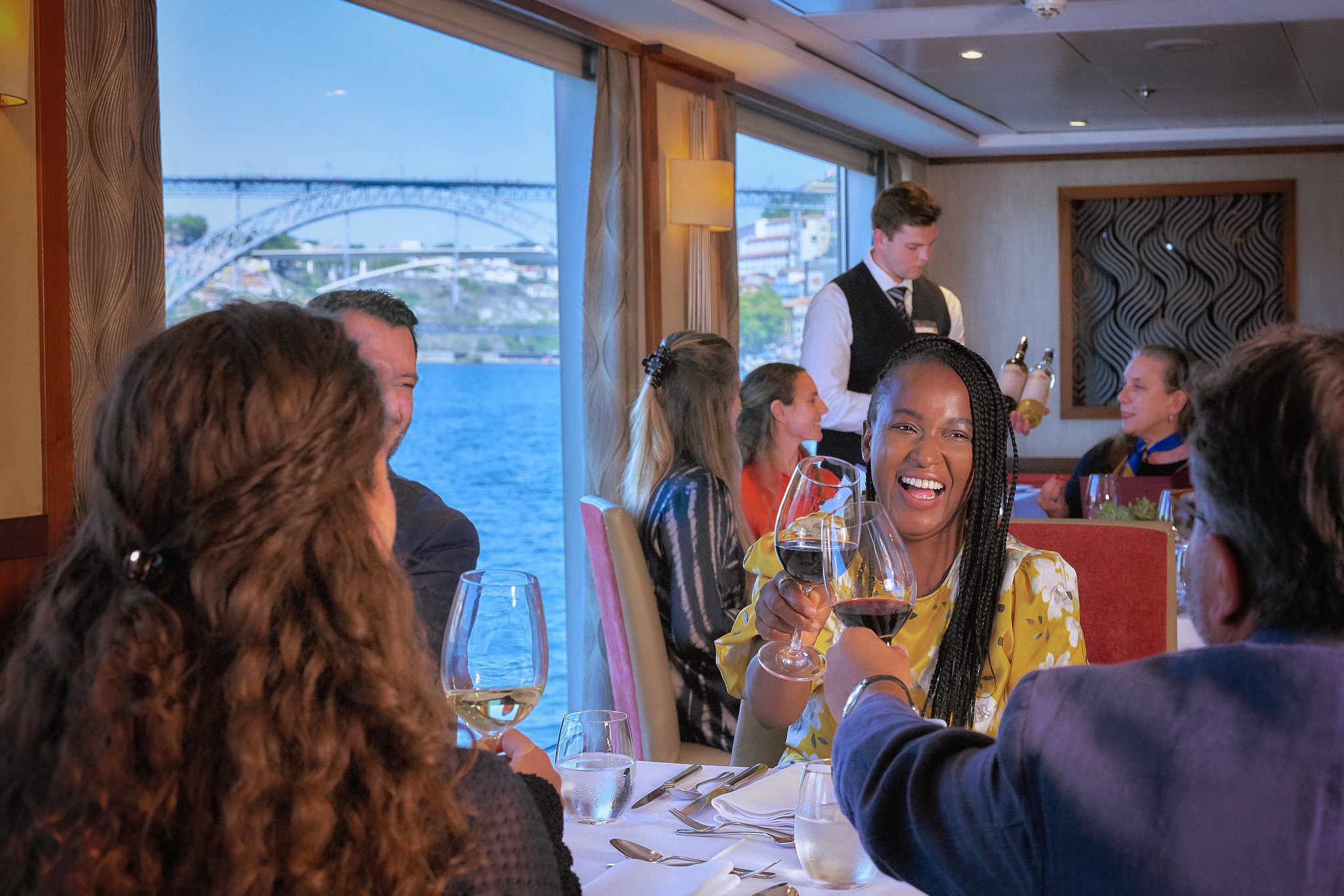 Group toasting with wine in a river cruise dining room, smiling woman in yellow
