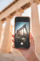 Hand holding smartphone capturing ancient temple columns visible on phone screen