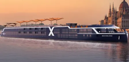 Sleek river cruise ship 'Boundless' with large X logo gliding by a riverside city skyline at sunset