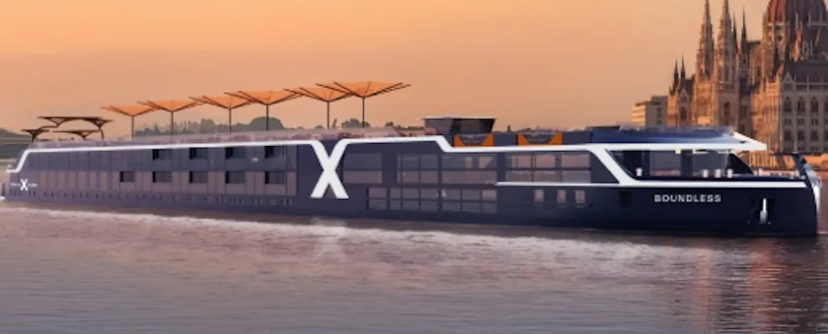 Sleek river cruise ship 'Boundless' with large X logo gliding by a riverside city skyline at sunset