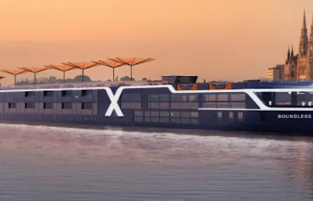 Sleek river cruise ship 'Boundless' with large X logo gliding by a riverside city skyline at sunset