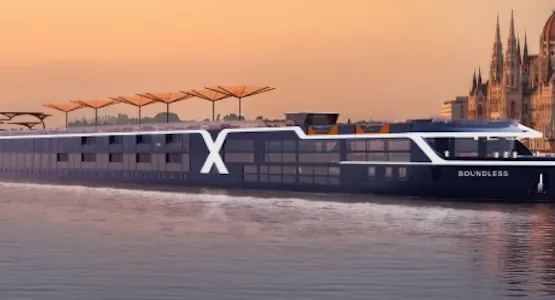 Sleek river cruise ship 'Boundless' with large X logo gliding by a riverside city skyline at sunset