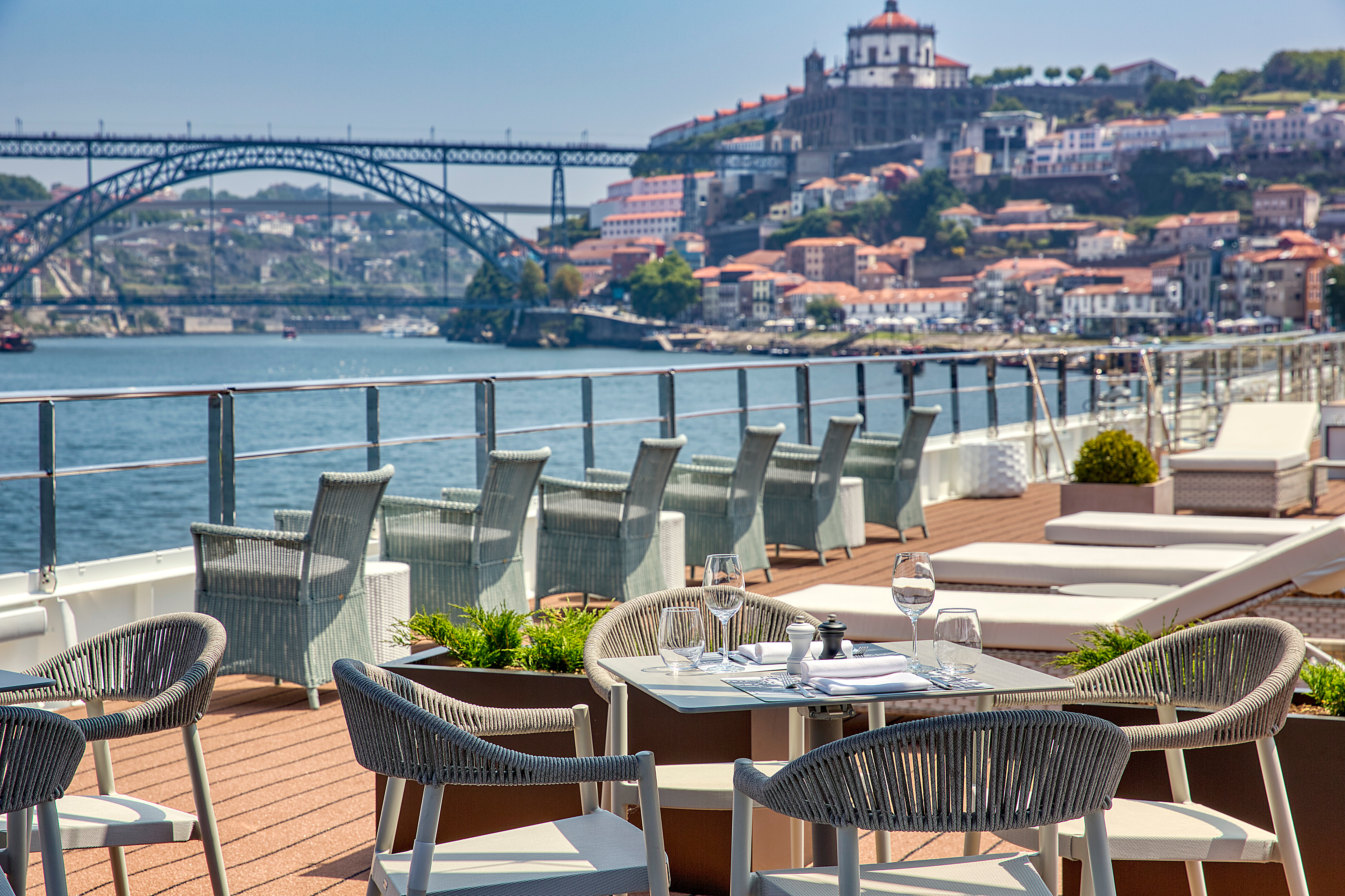 Riverside terrace dining with set table, wicker chairs and arched bridge view