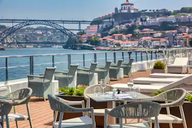 Riverside terrace dining with set table, wicker chairs and arched bridge view