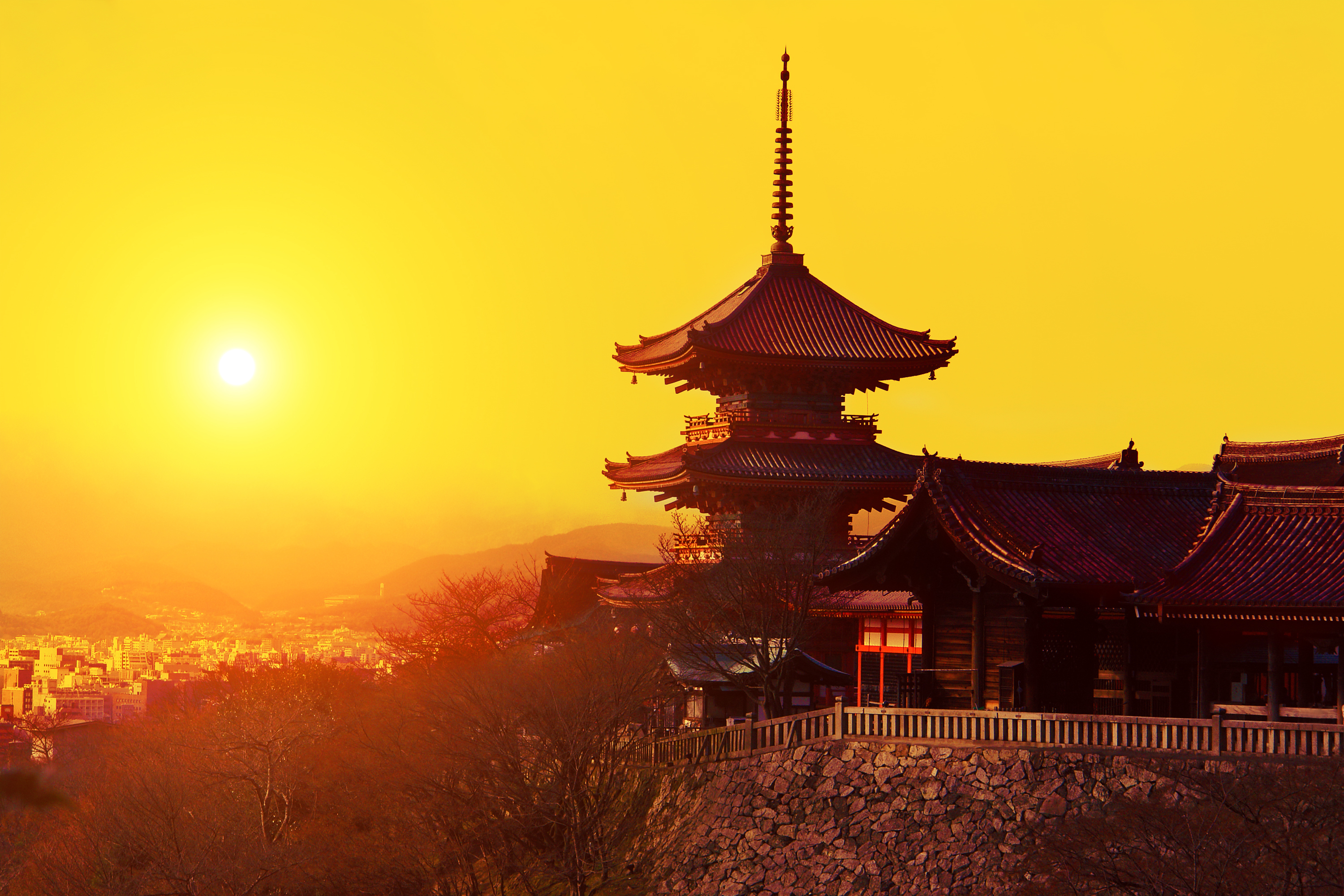 Traditional multi-tiered temple pagoda silhouetted against golden sunset, overlooking a city.