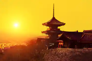 Traditional multi-tiered temple pagoda silhouetted against golden sunset, overlooking a city.