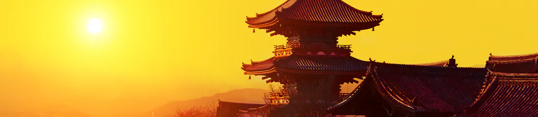 Traditional multi-tiered temple pagoda silhouetted against golden sunset, overlooking a city.