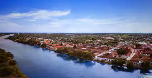 Aerial panorama of colonial riverside town with red-tiled roofs, riverside trees, and church tower