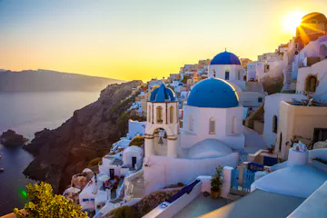 Sunset over Santorini cliffside village with white houses and blue-domed churches
