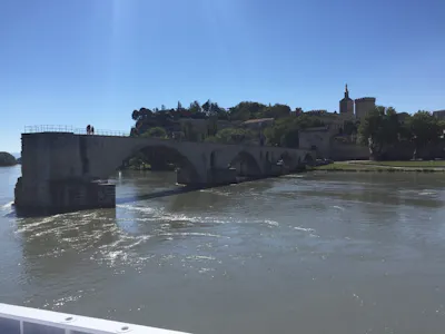 Stone arched bridge over the Rhône with pedestrians, riverside trees and medieval buildings