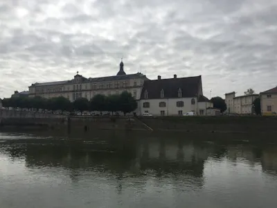 Riverside historic building with dome and tree-lined quay reflected in river