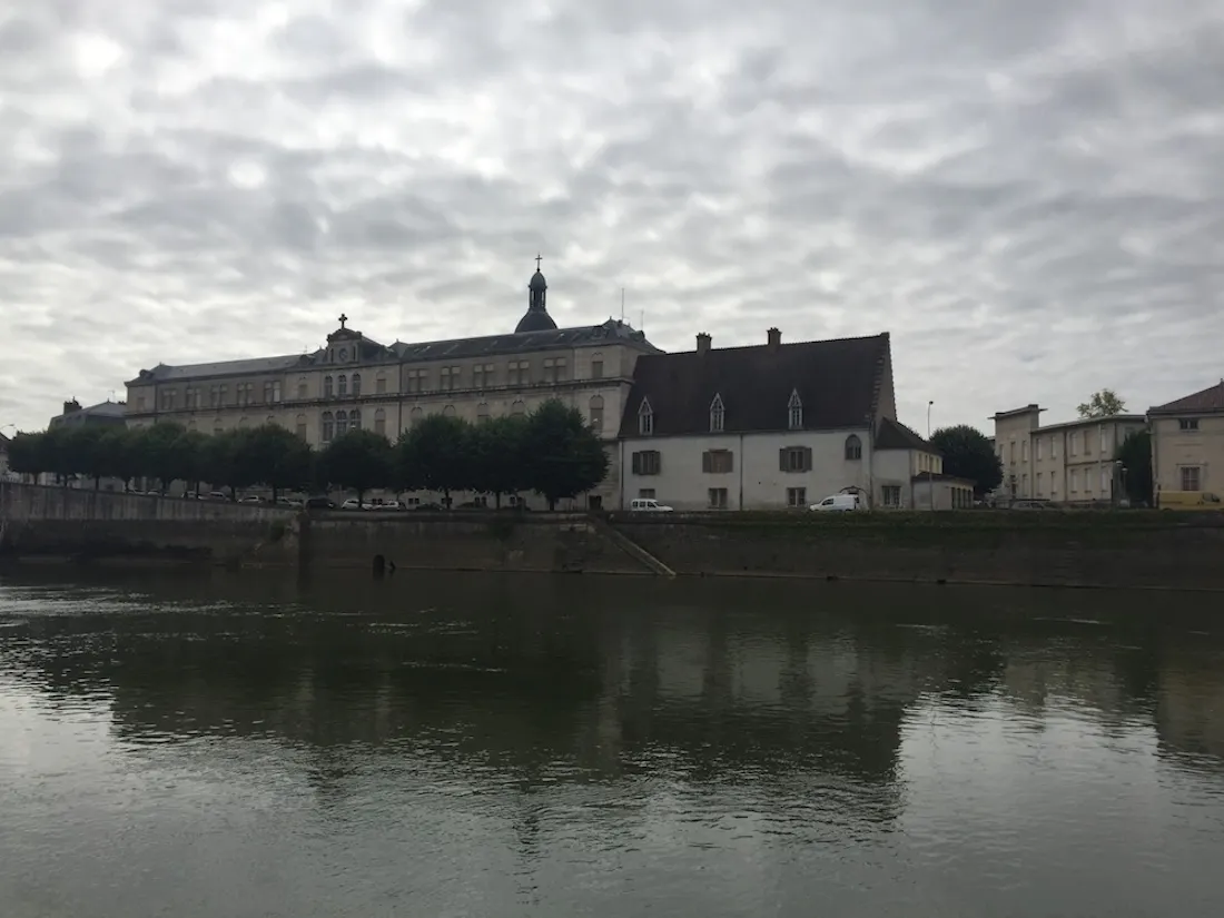 Riverside historic building with dome and tree-lined quay reflected in river