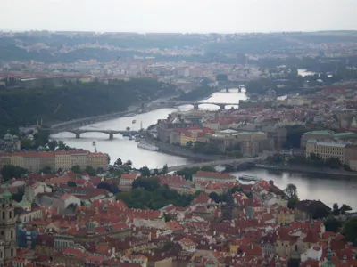 Aerial cityscape of Prague's Vltava River with bridges, boats, and red‑roofed buildings