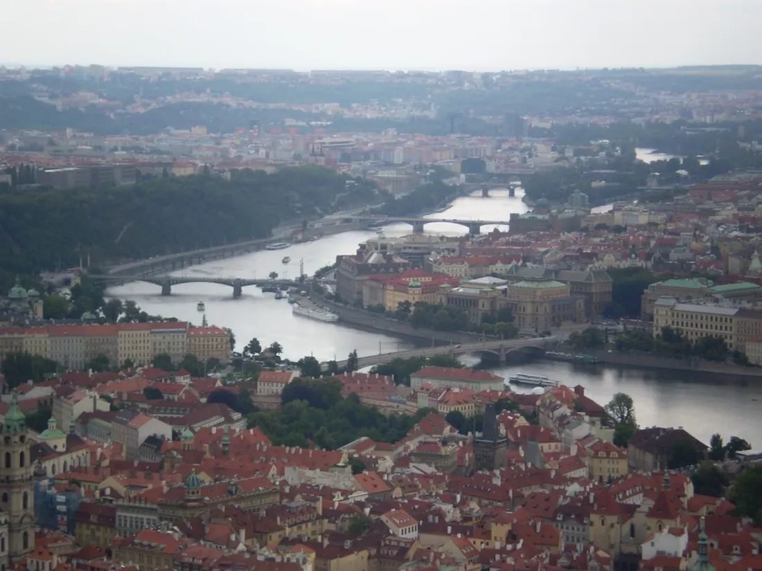 Aerial cityscape of Prague's Vltava River with bridges, boats, and red‑roofed buildings
