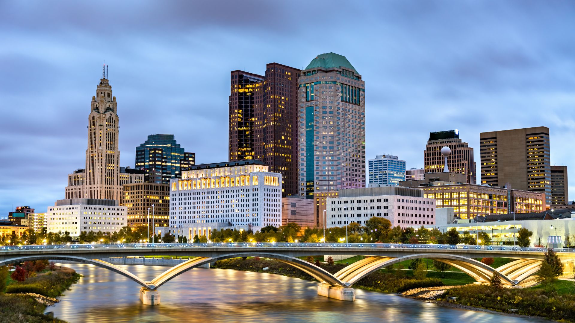 Columbus, Ohio skyline at dusk with illuminated downtown towers and arched river bridge