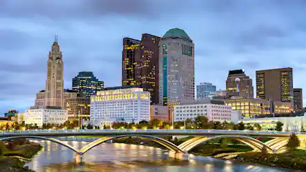 Columbus, Ohio skyline at dusk with illuminated downtown towers and arched river bridge