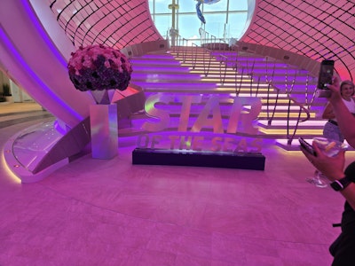 LED-lit curved staircase atrium photo spot with floral display and sign 'STAR'.