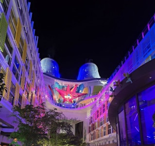 Nighttime cruise ship promenade lit in neon, twin blue funnels and central red star sculpture