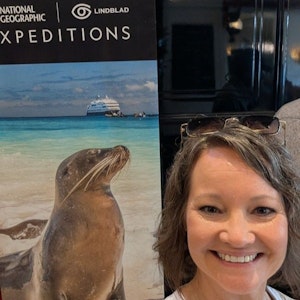 Smiling woman next to National Geographic Lindblad Expeditions poster with sea lion and ship
