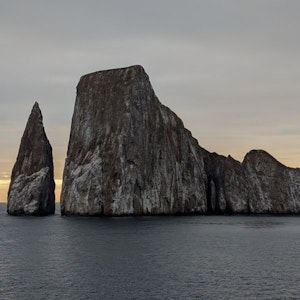 Narrow sea stack and flat-topped monolith rising from ocean at dusk