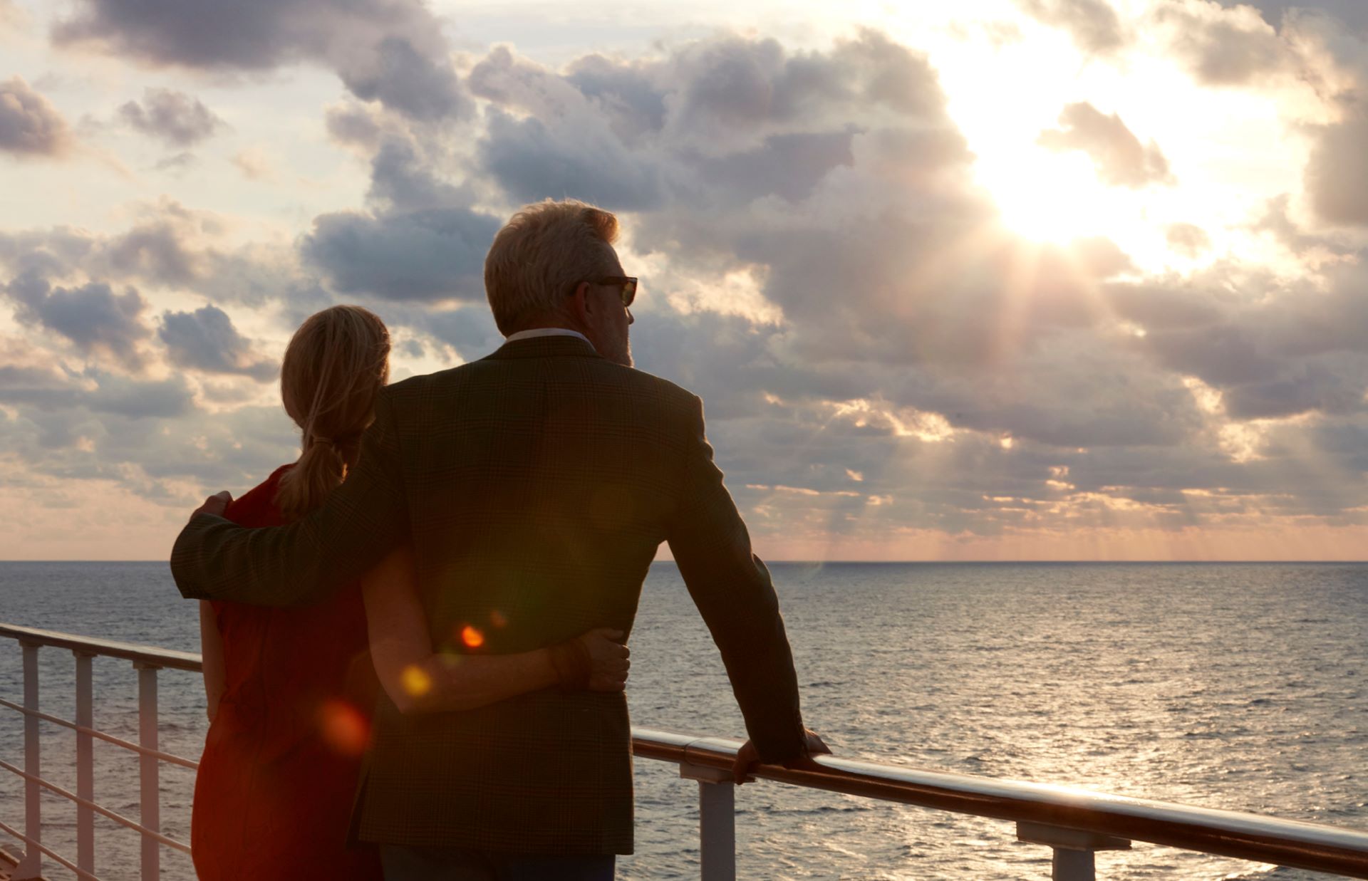 Couple embracing on ship deck watching sunlit clouds over the ocean