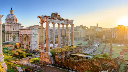 Sunrise over the Roman Forum with tall temple columns, ancient ruins and a church dome