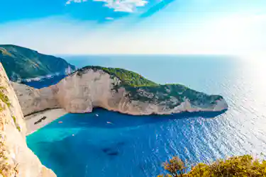 Clifftop view of turquoise bay, sandy beach with shipwreck, and limestone arch