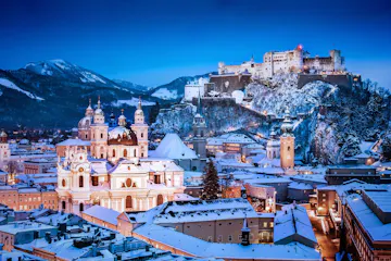 Snow-covered Salzburg skyline at dusk with cathedral domes and Hohensalzburg Fortress