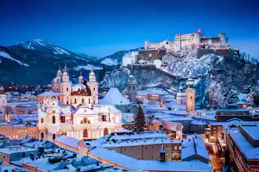 Snow-covered Salzburg skyline at dusk with cathedral domes and Hohensalzburg Fortress