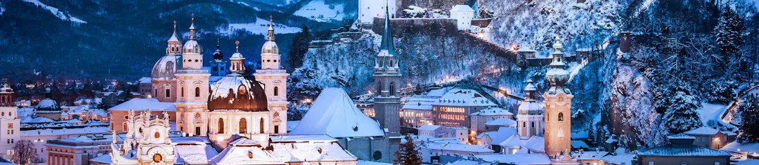 Snow-covered Salzburg skyline at dusk with cathedral domes and Hohensalzburg Fortress