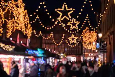 Nighttime Christmas market street with star-shaped lights strung above festive stalls and crowds.