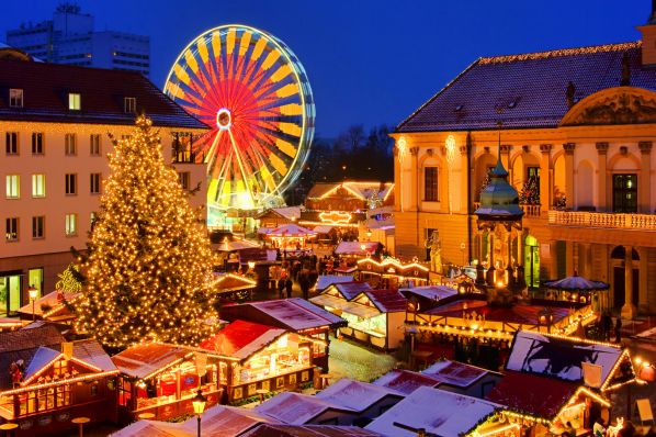 Nighttime Christmas market with lit fir tree, festive stalls, glowing Ferris wheel, old buildings