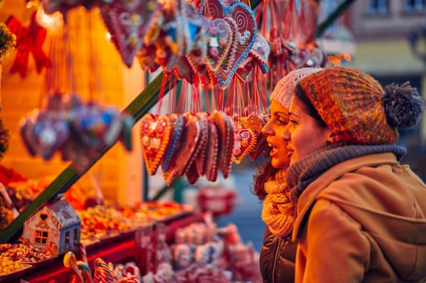 Two women in knit hats view hanging heart-shaped gingerbread at a holiday market stall