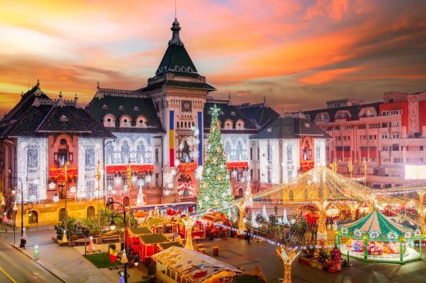 Town square Christmas market at dusk with illuminated historic city hall, lit tree and carousel.