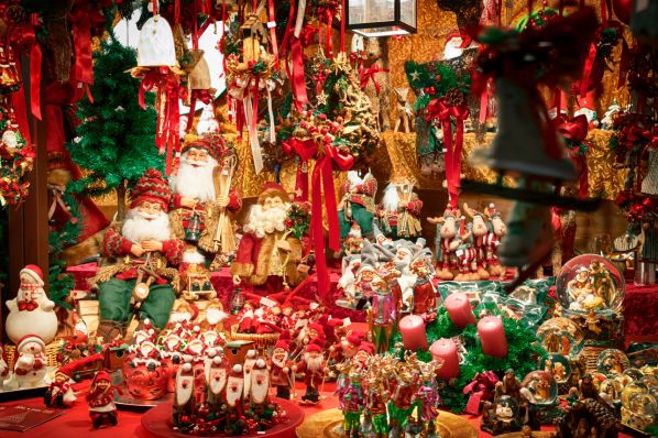 Christmas market stall crowded with Santa figurines, ornaments, wreaths, candles, red ribbons