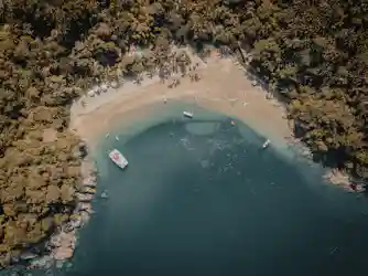 Aerial view of curved tropical beach with palm trees, umbrellas and boats in turquoise bay