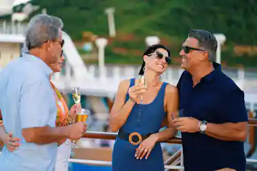 Two couples on a cruise deck wearing sunglasses, smiling and toasting with champagne.