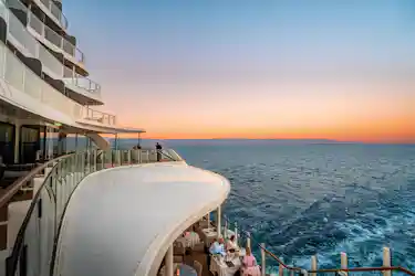 Curved cruise ship balconies with glass railings and diners overlooking ocean at sunset