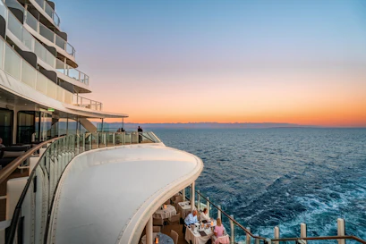 Curved cruise ship balconies with glass railings and diners overlooking ocean at sunset