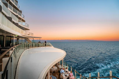 Curved cruise ship balconies with glass railings and diners overlooking ocean at sunset